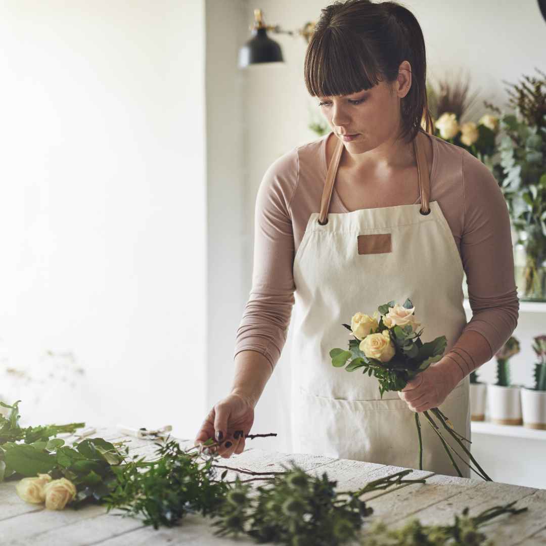 Floristin am Bindetresen mit verschiedenen Blumen vor sich liegend.