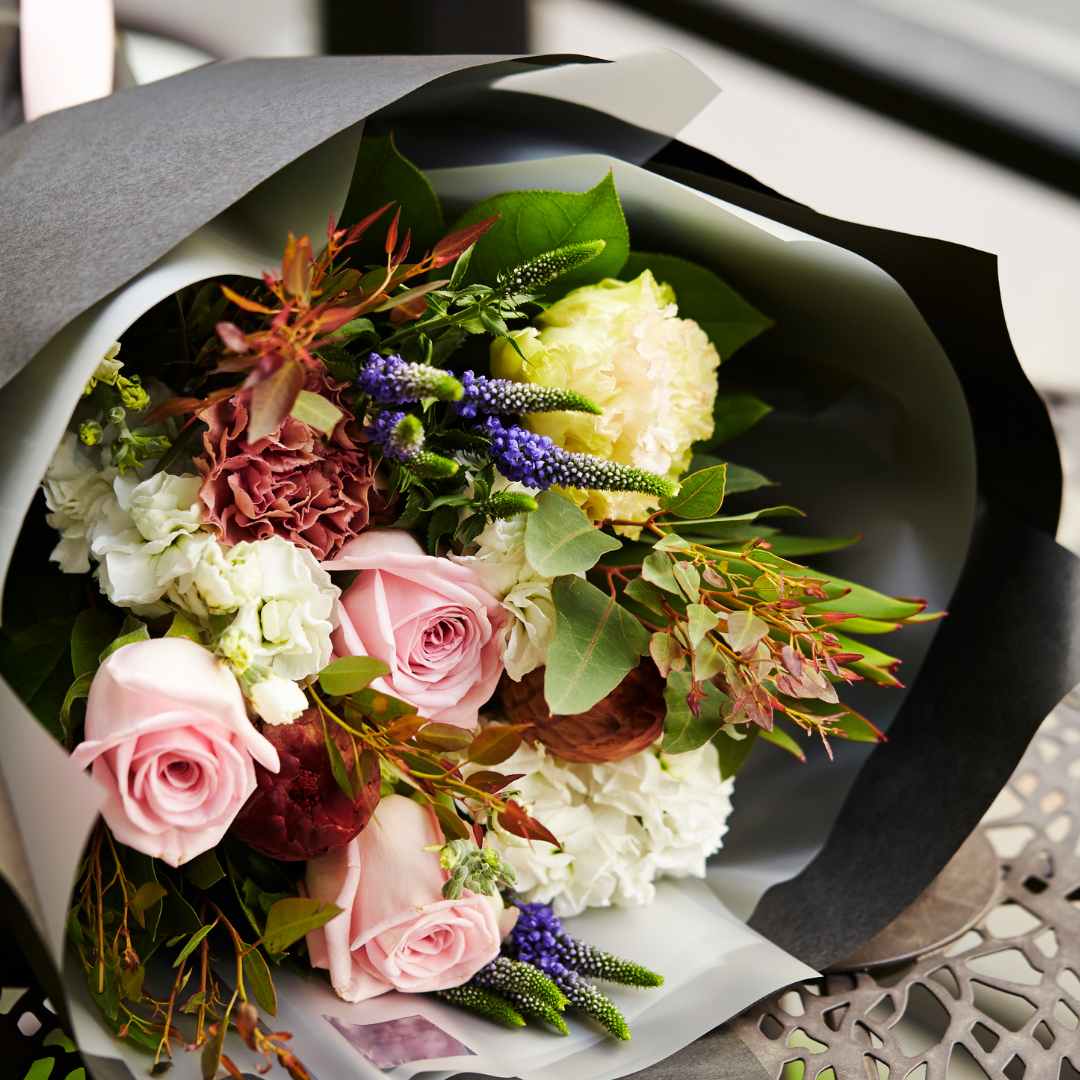 Farbenfroher Blumenstrauß, eingepackt in grau-schwarzem Seidenpapier, auf dem Tisch liegend.
