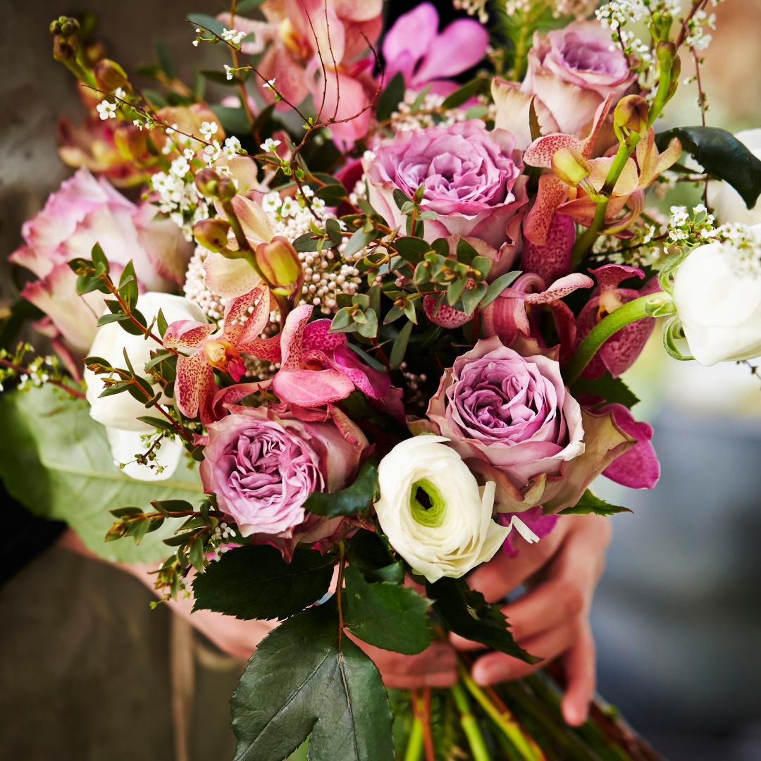 Nahaufnahme eines fertigen Blumenstraußes mit rosafarbenen Rosen, Schmertterlingsorchidee, weißer Pon-Pon Ranunkel und Beiwerk.