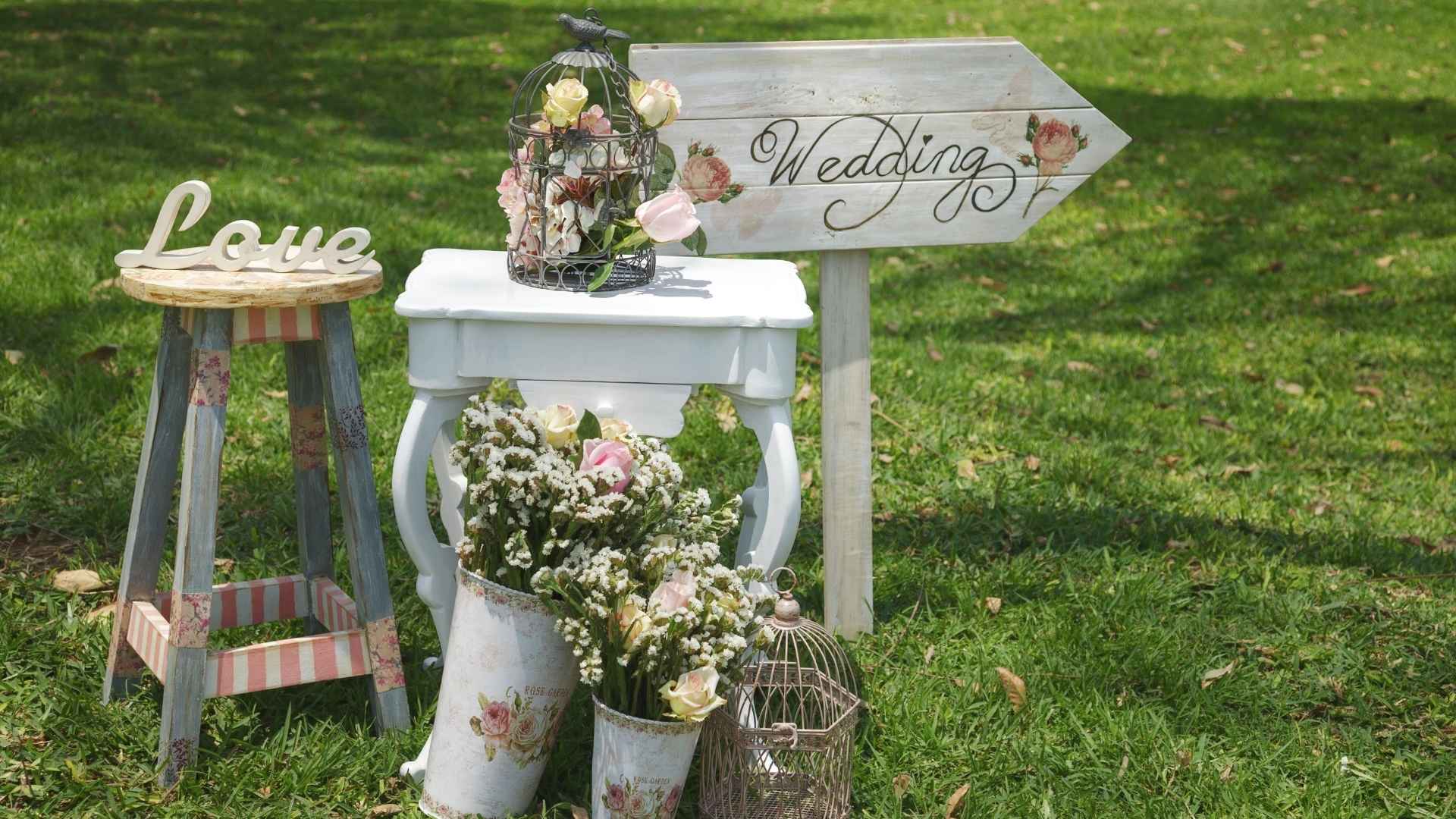 Wiese mit Wegweiser zur Hochzeit, dazu Blumendeko und ein paar alte Möbelstücke